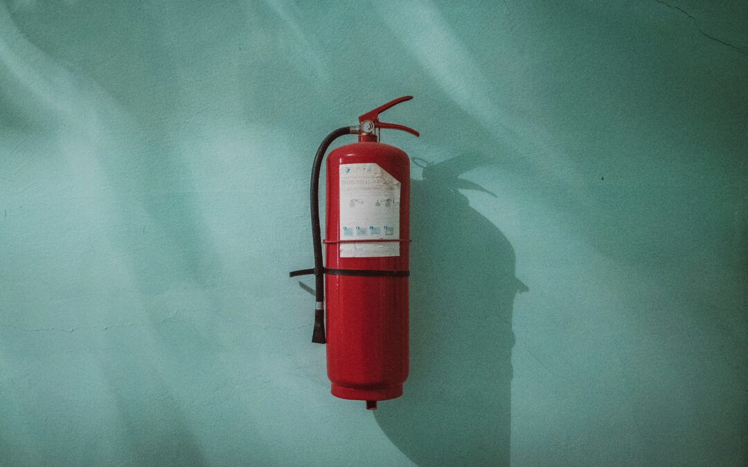 red fire extinguisher hanging on blue green wall